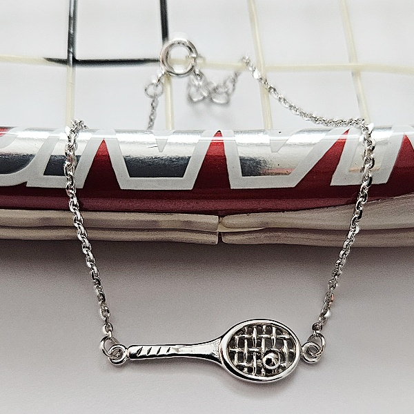 Detailní pohled na stříbrný tenisový náramek s raketou a míčkem